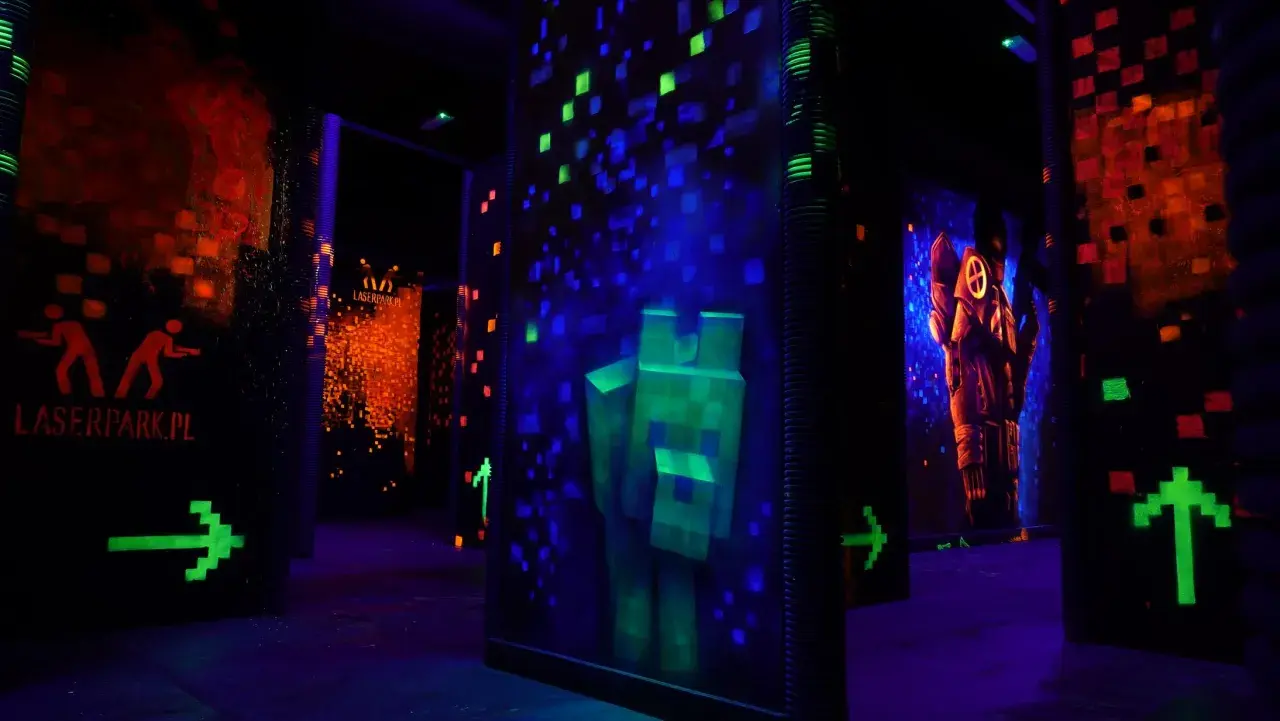 Mroczna arena do laser tag z neonowymi grafikami, strzałkami i postaciami.