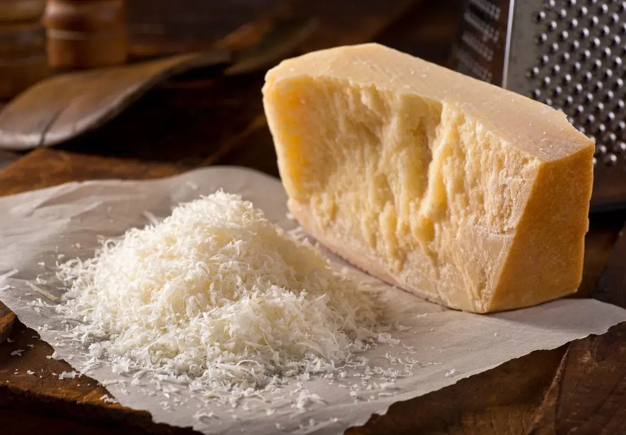 Un pezzo di Parmigiano Reggiano accanto a una montagnetta di formaggio grattugiato. Si può congelare il parmigiano grattugiato per averlo sempre pronto.