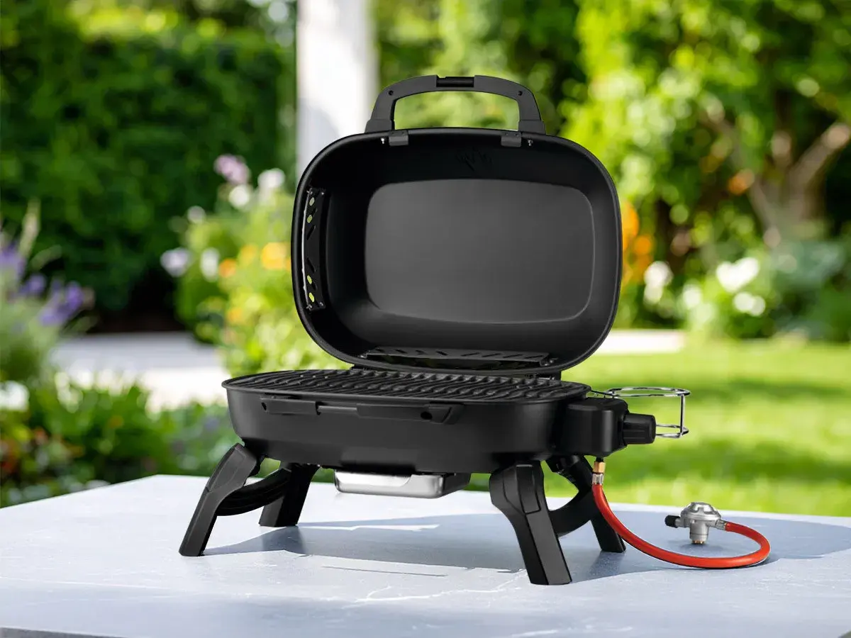 Barbecue à gaz portable, ouvert, avec couvercle, prêt pour de délicieuses recettes barbecue gaz avec couvercle dans un jardin ensoleillé.