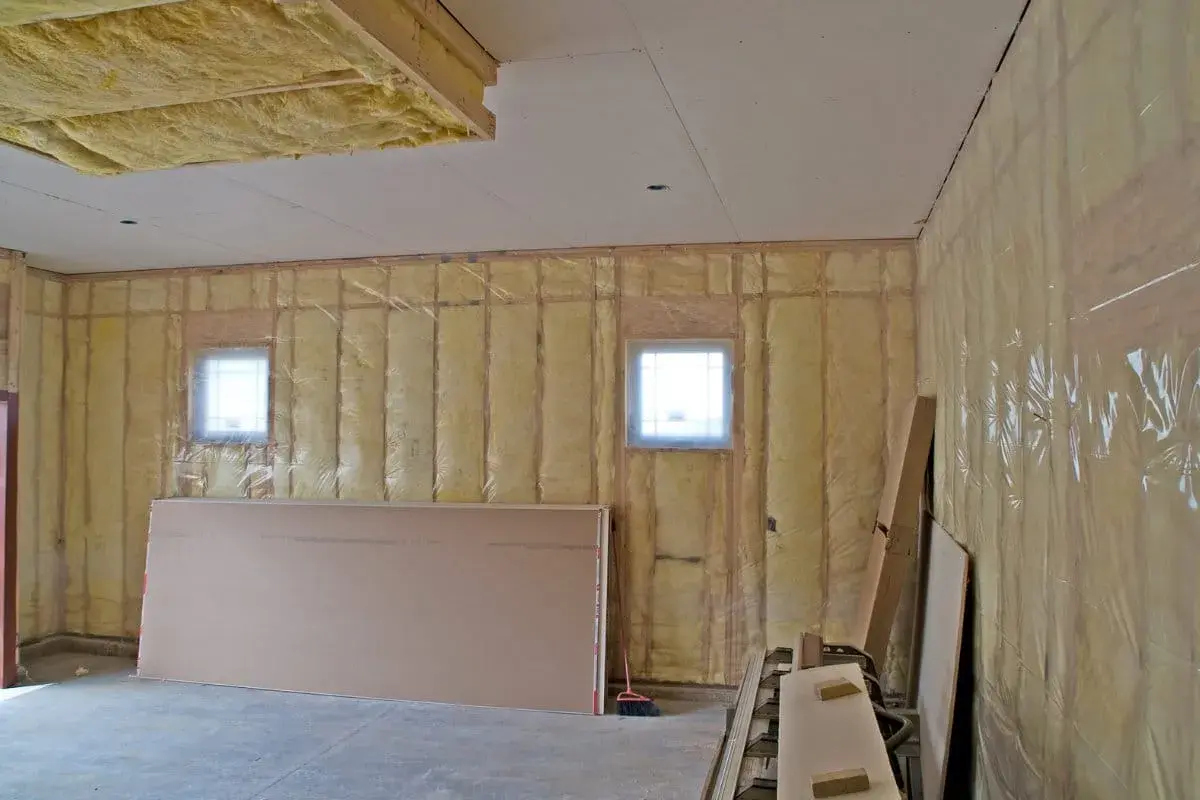 Travaux en cours pour isoler un garage non chauffé. Isolation jaune visible sur les murs et le plafond, avec des plaques de plâtre et des fenêtres.