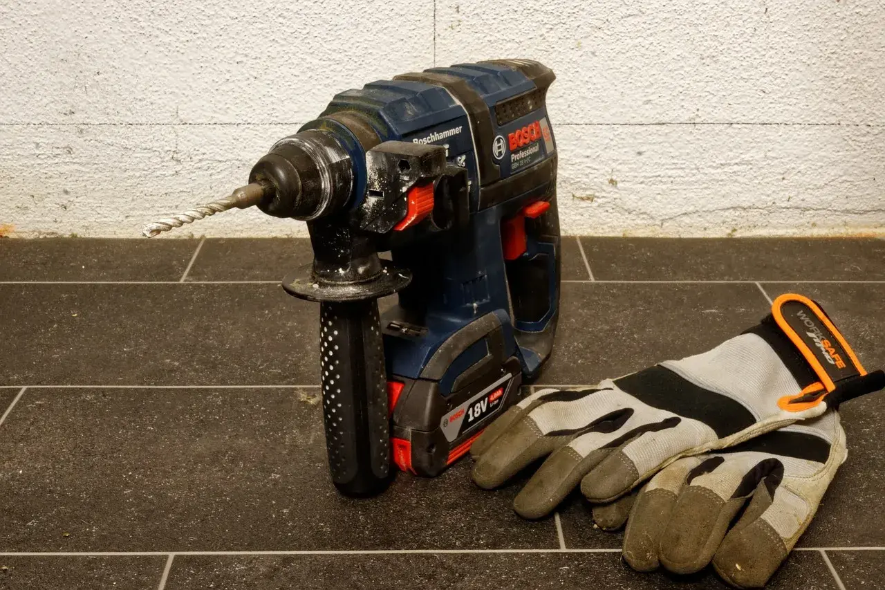 Mocna wiertarka udarowa Bosch z zamontowanym wiertłem i rękawicami roboczymi obok. Dowiedz się, jak wyjąć wiertło z wiertarki.