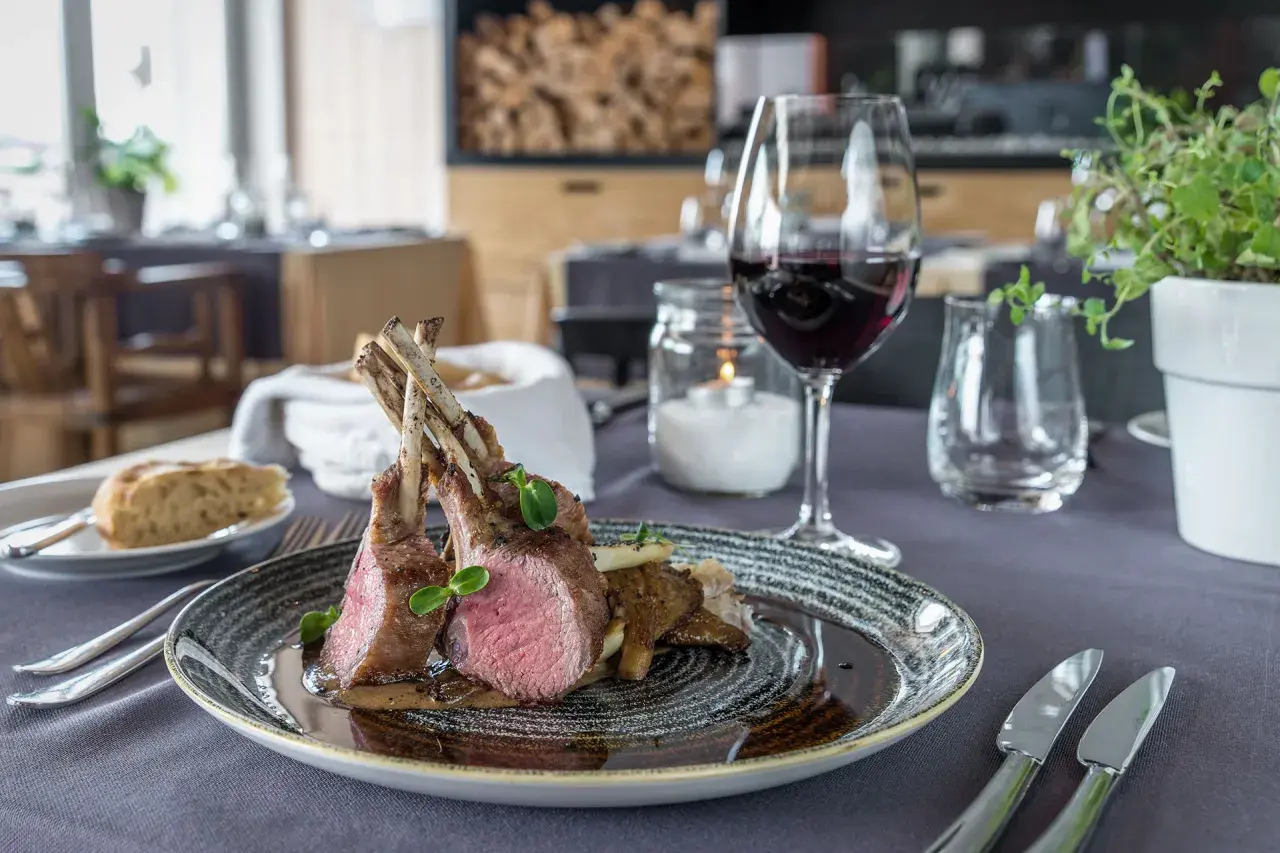 Carré d'agnello al forno con funghi e un bicchiere di vino rosso, un abbinamento perfetto per un pasto speciale.
