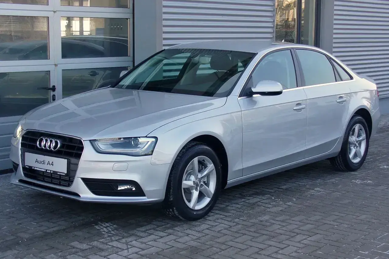 Srebrny Audi A4 B8, model znany z typowych usterek, stoi przed budynkiem.