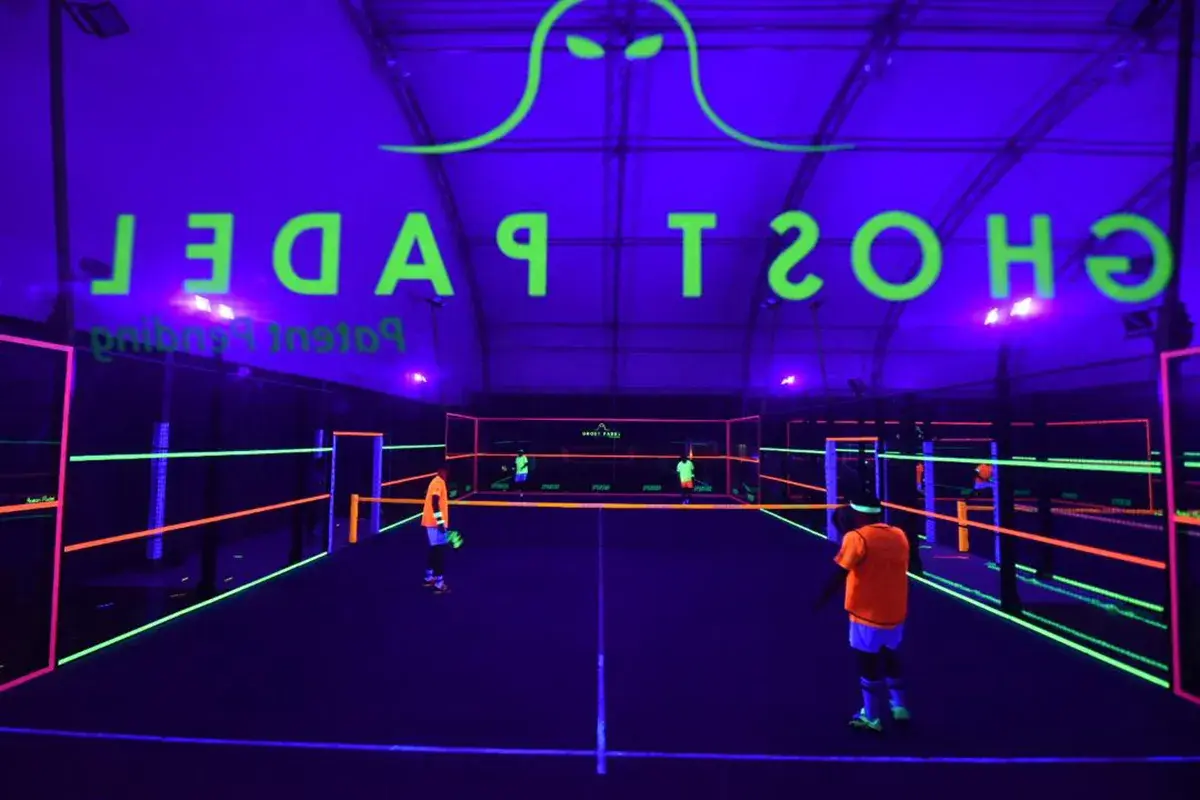 Campo da padel al neon con logo "Ghost Padel" e giocatori in azione.