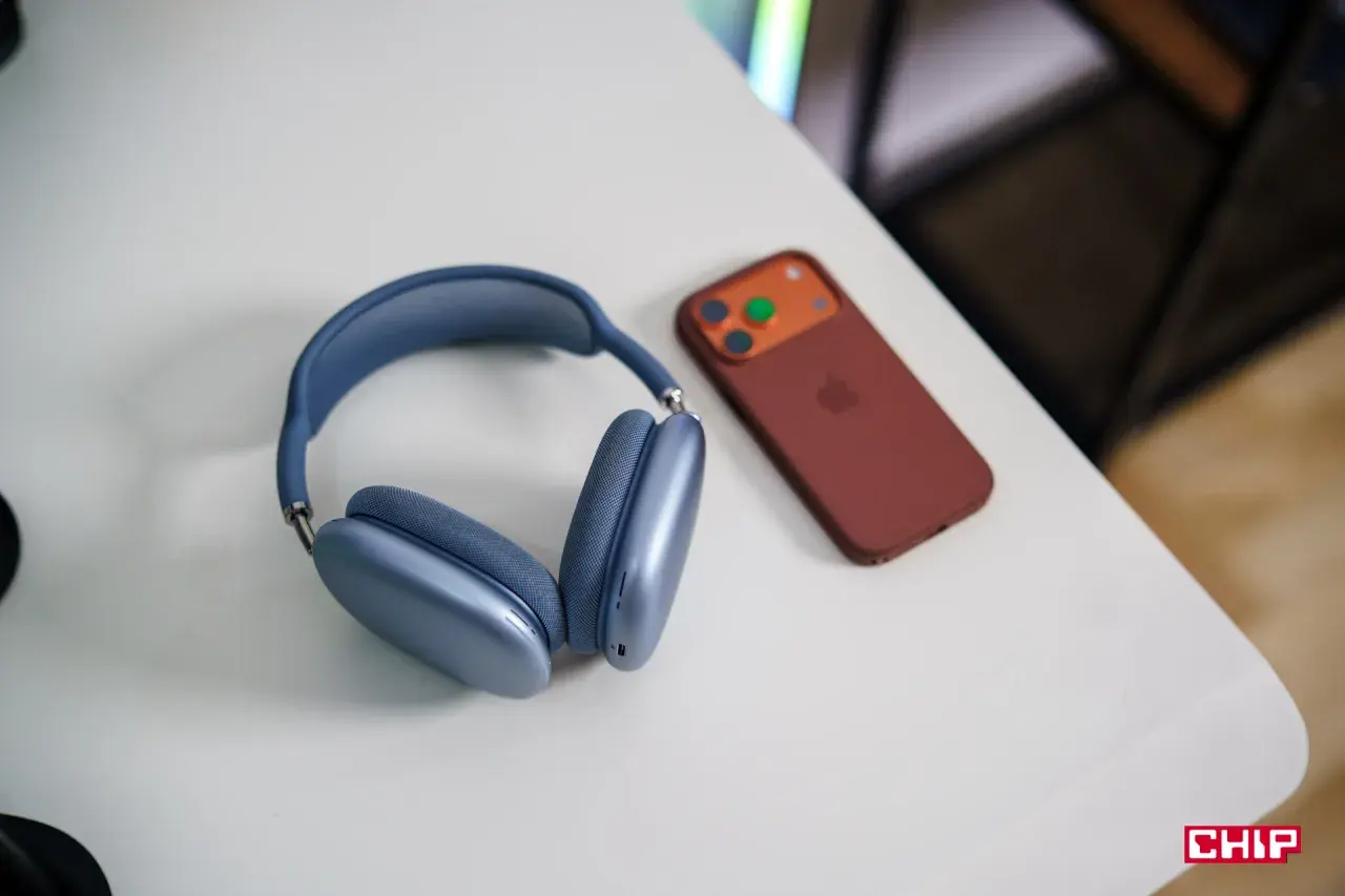 Niebieskie słuchawki AirPods Max i brązowy iPhone na białym biurku. Dowiedz się, jak połączyć AirPods z PC.
