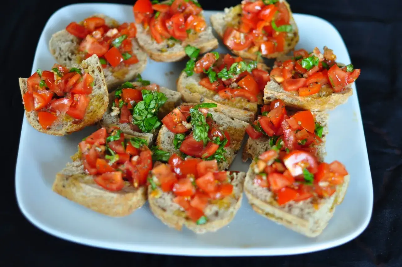Bruschetta z pomidorami i bazylią, ułożona na białym talerzu. Chrupiące grzanki z dodatkiem świeżych, soczystych pomidorów i aromatycznej bazylii.