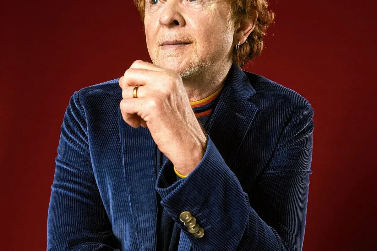 Mężczyzna z rudymi włosami, w granatowej sztruksowej marynarce, z dłonią na brodzie. To wokalista Simply Red.