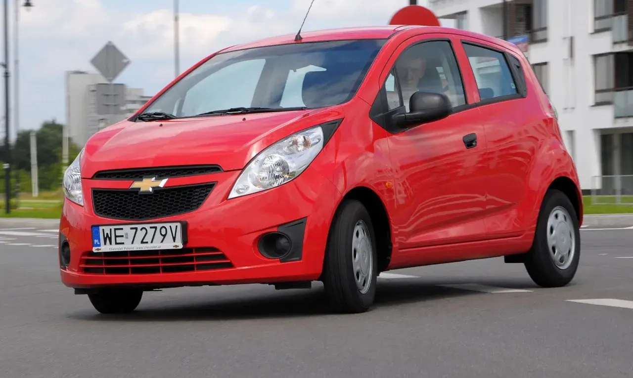 Czerwony Chevrolet Spark na drodze. Kierowca w środku. Wiele osób szuka chevrolet spark opinie przed zakupem.