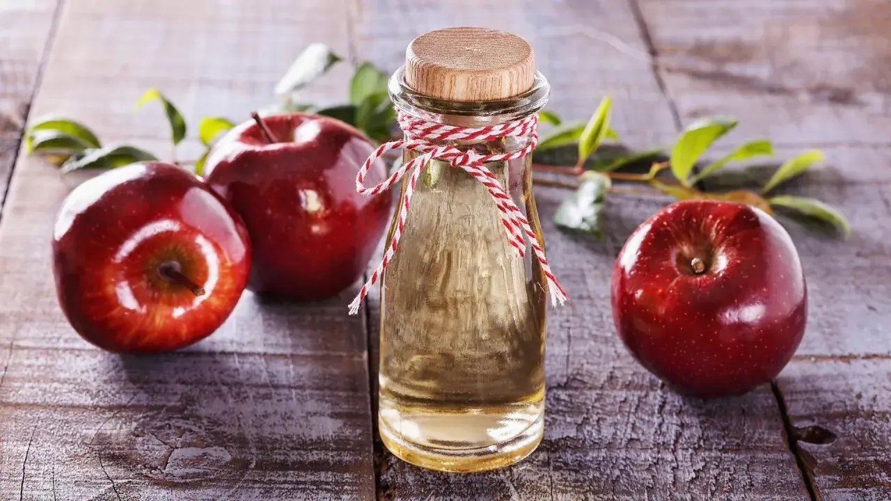 Rote Äpfel und eine Flasche Apfelessig auf Holz. Die natürliche Apfelessig Wirkung auf die Haut ist ein Geheimnis der Schönheit.