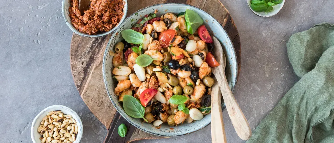 Gnocchi-Salat mit Pesto, Tomaten, Oliven und Pinienkernen in einer Schüssel.