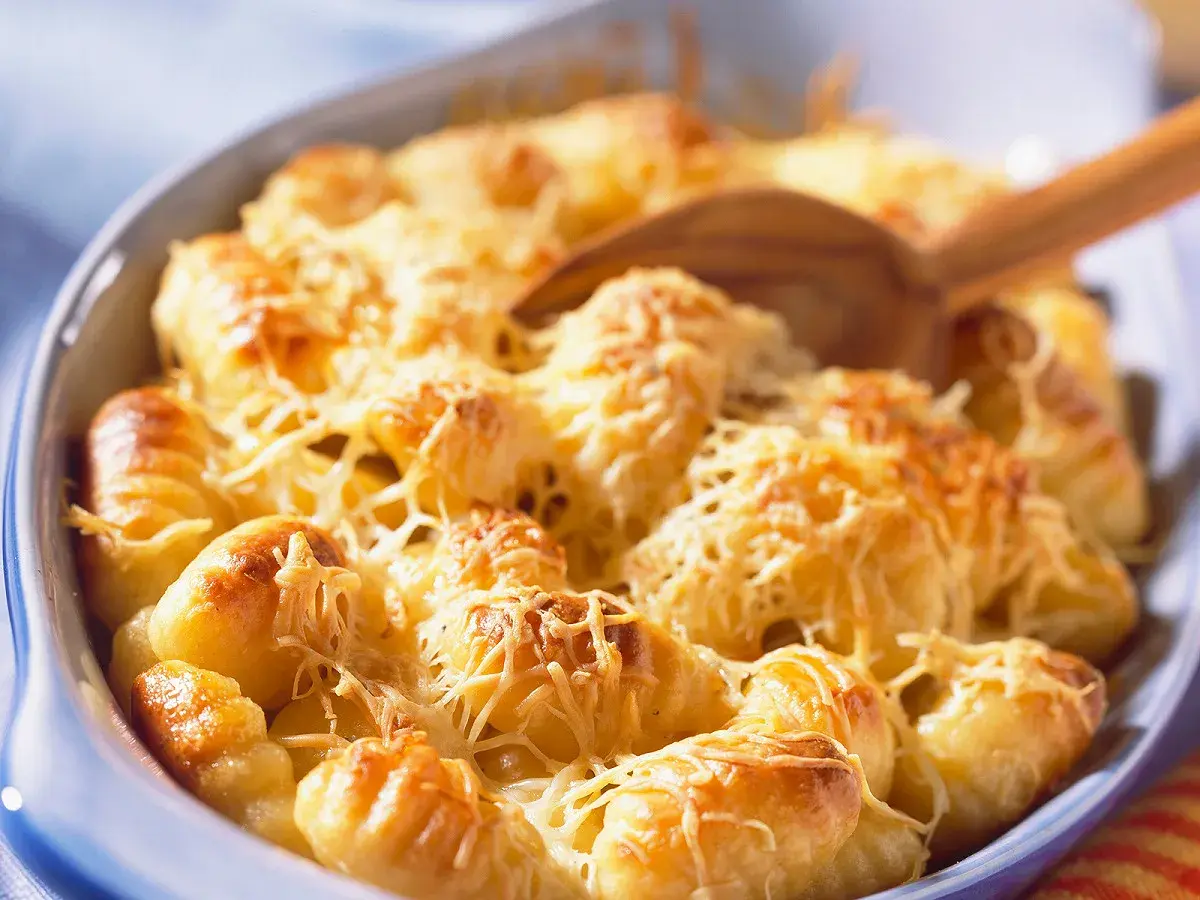 Un plat de gratin de gnocchi doré et gratiné au fromage, prêt à être servi avec une cuillère en bois.