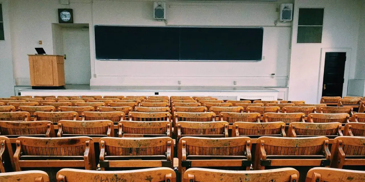 Aula vacía con asientos de madera y pizarra. Un profesor podría hablar aquí, pero para explicar la diferencia entre speak y talk, necesitaría a los estudiantes.