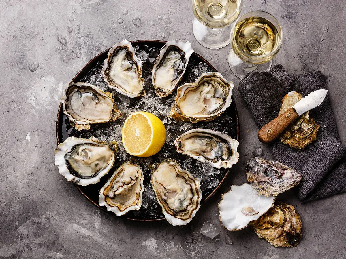 Plateau d'huîtres fraîches avec citron, deux verres de vin blanc, parfait pour le meilleur vin blanc pour fruits de mer.