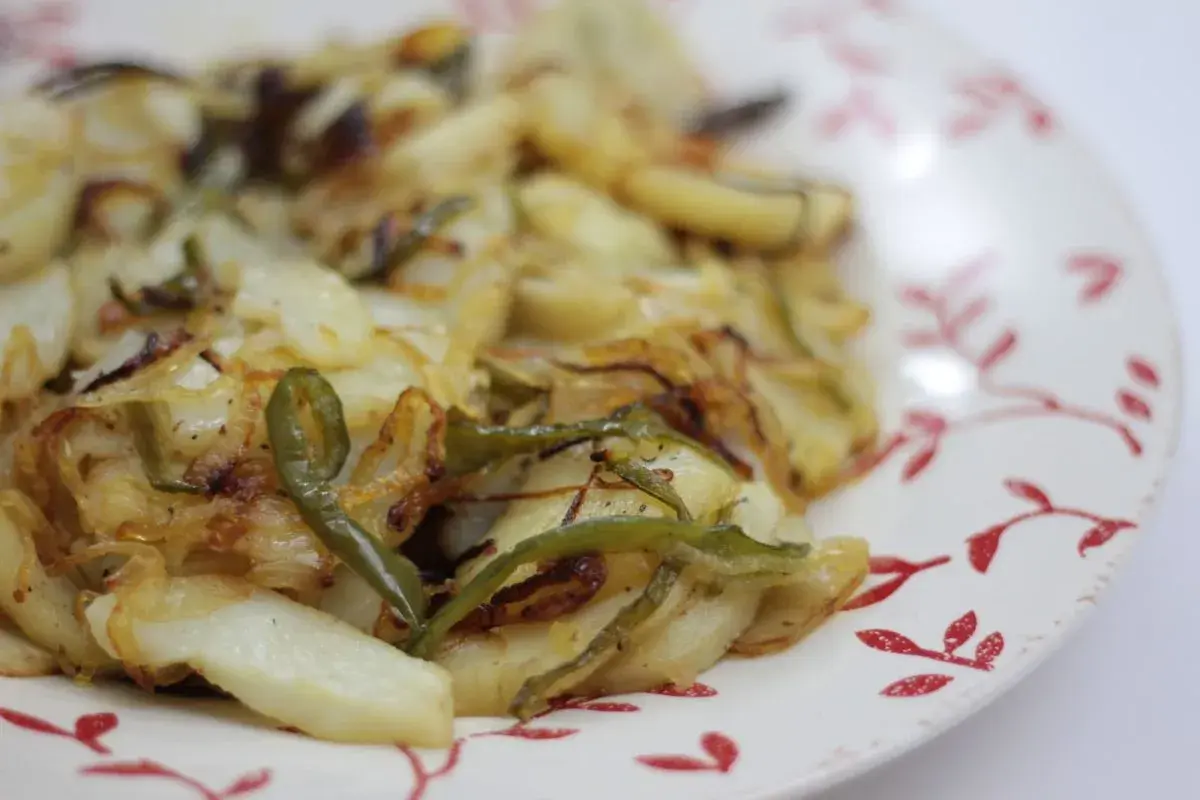 Plato de patatas panaderas al horno con cebolla y pimientos verdes, recién sacadas del horno y listas para disfrutar.