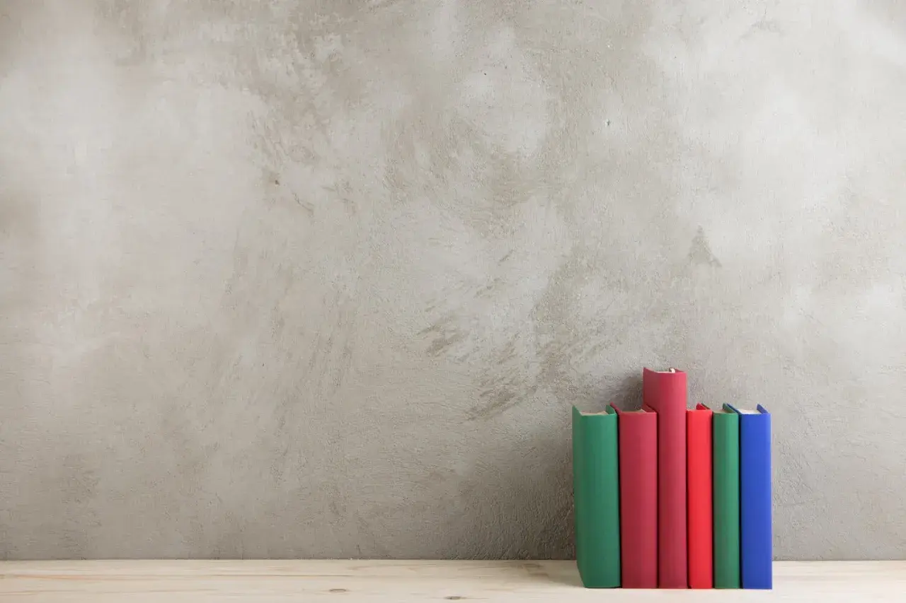 Bunte Bücher stehen vor einer Wand in Beton Optik.