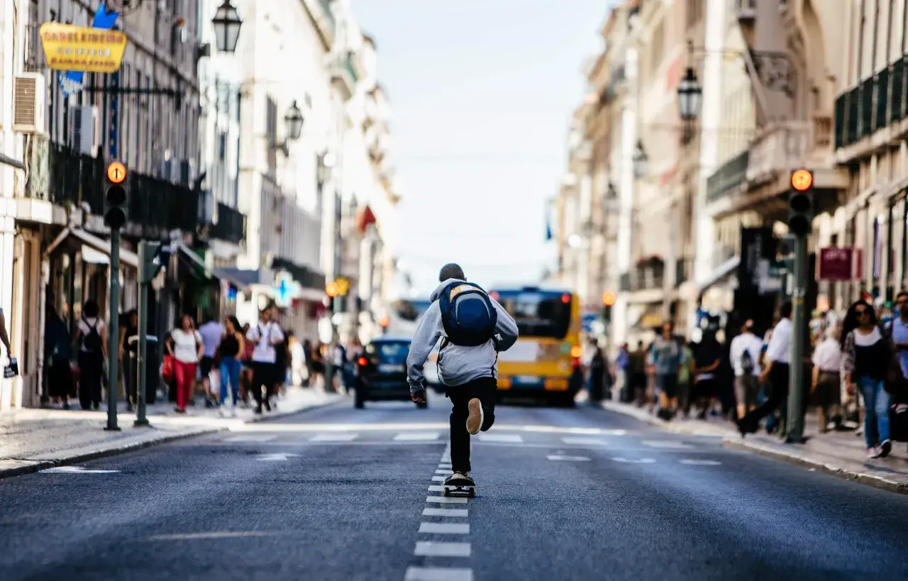 Chłopak na deskorolce przemierza ruchliwą ulicę w ramach miejskiej fotografii. W tle widać ludzi i żółty autobus.