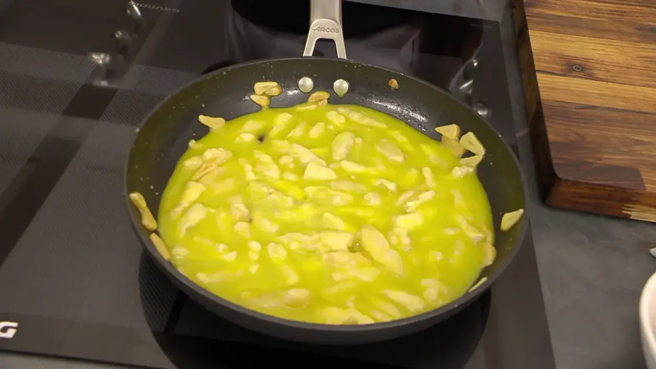 El bacalao al pil pil burbujea en la sartén, con trozos de ajo dorándose en el aceite.