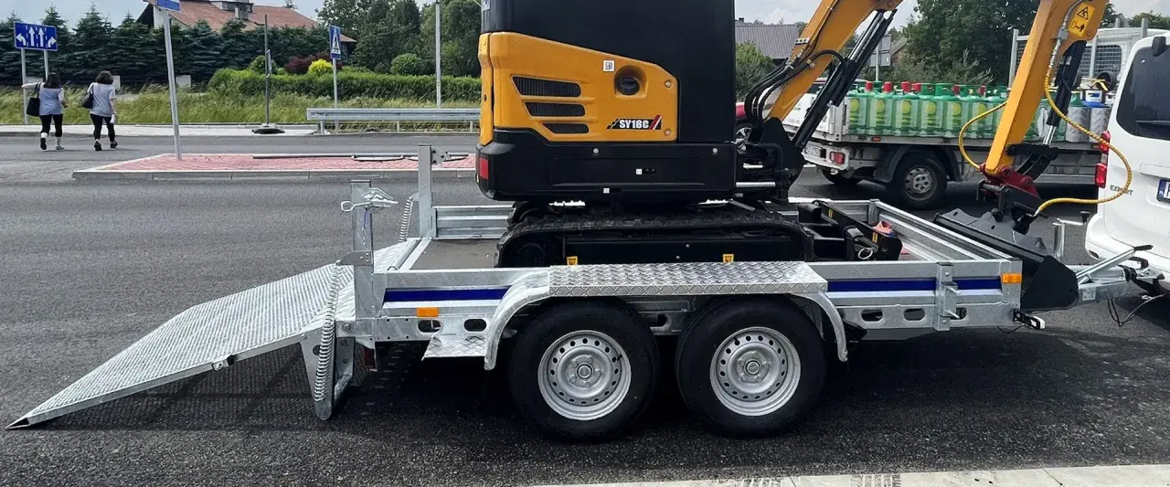 Żółta mini koparka SY18C na przyczepie z rampą. Waga maszyny pozwala na łatwy transport.