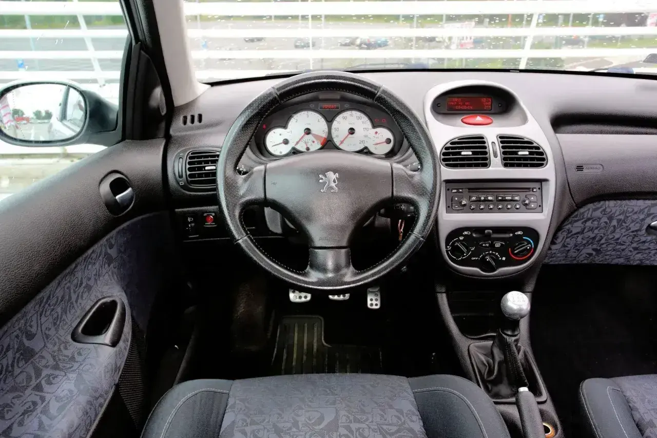 Wnętrze Peugeota 206 1.4 benzyna. Widok na deskę rozdzielczą, kierownicę z logo lwa, radio i dźwignię zmiany biegów.