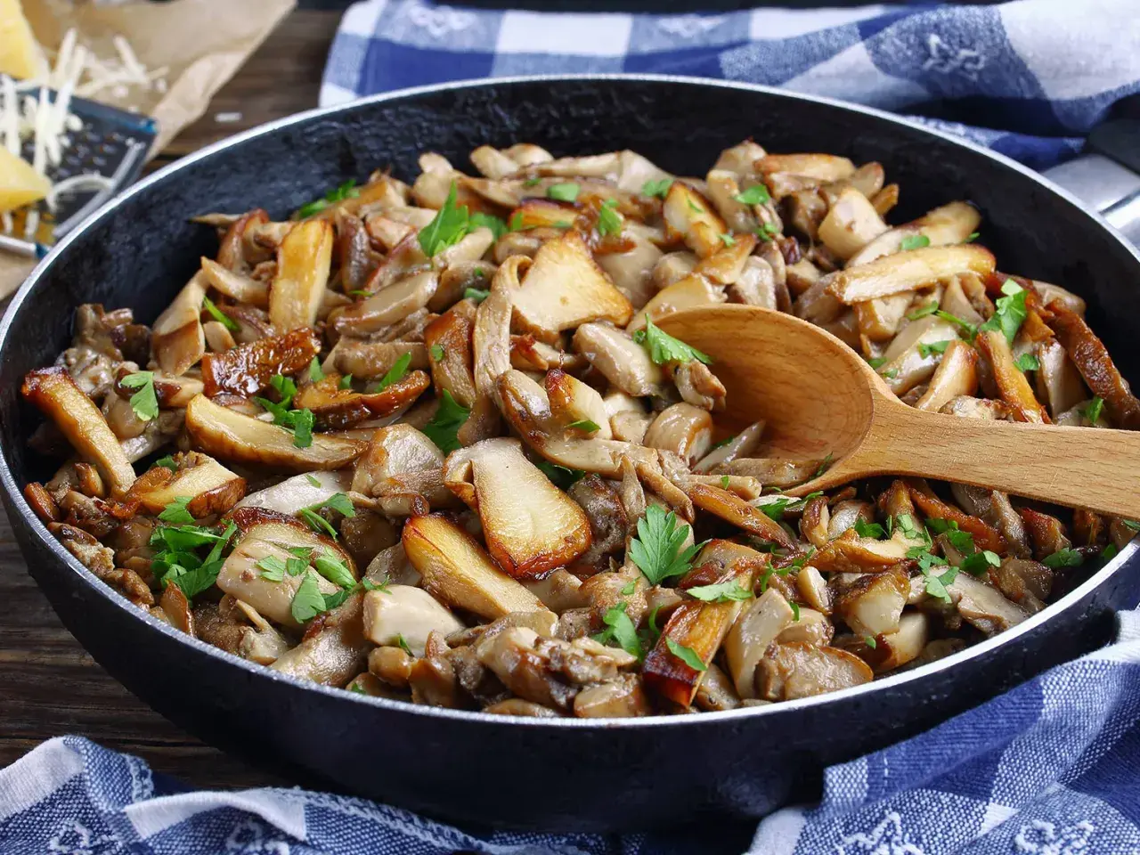 Une poêle débordante de fondue savoyarde aux cèpes, garnie de persil frais. Une cuillère en bois repose sur ce délice forestier.