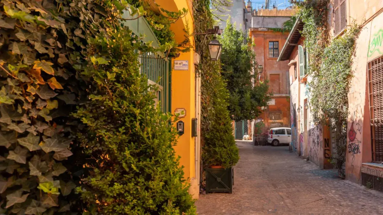 Un vicolo pittoresco tra le vie di Roma centro, con edera rampicante, edifici colorati e un'auto bianca parcheggiata.