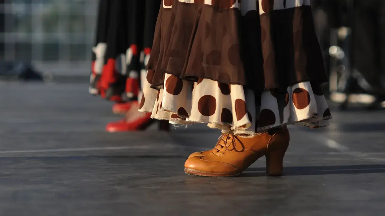 Taconeo flamenco: un zapato de cuero marrón con cordones y tacón, parte de un vestido de lunares, listo para bailar.