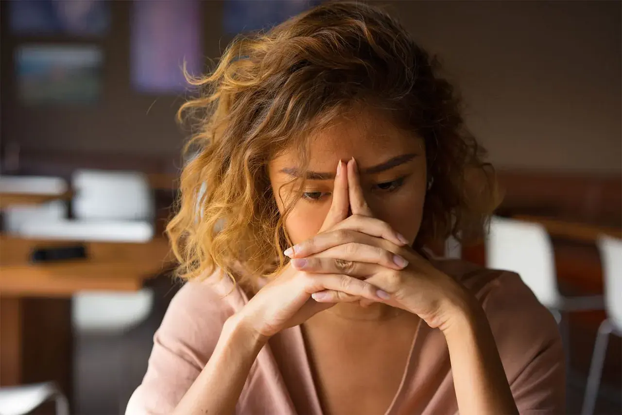 Een vrouw met haar handen voor haar gezicht, die zich terugtrekt uit de wereld. Ze lijkt overgevoelig voor geluid en prikkels, zoekend naar rust.
