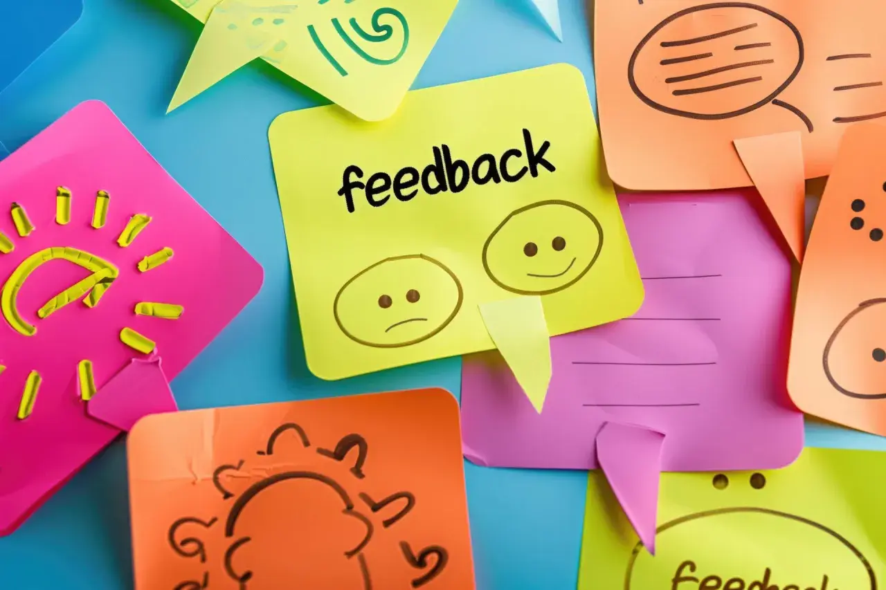 Kolorowe karteczki z rysunkami i napisem "feedback". Jedna pokazuje smutną i wesołą buźkę, symbolizując konstruktywny feedback.