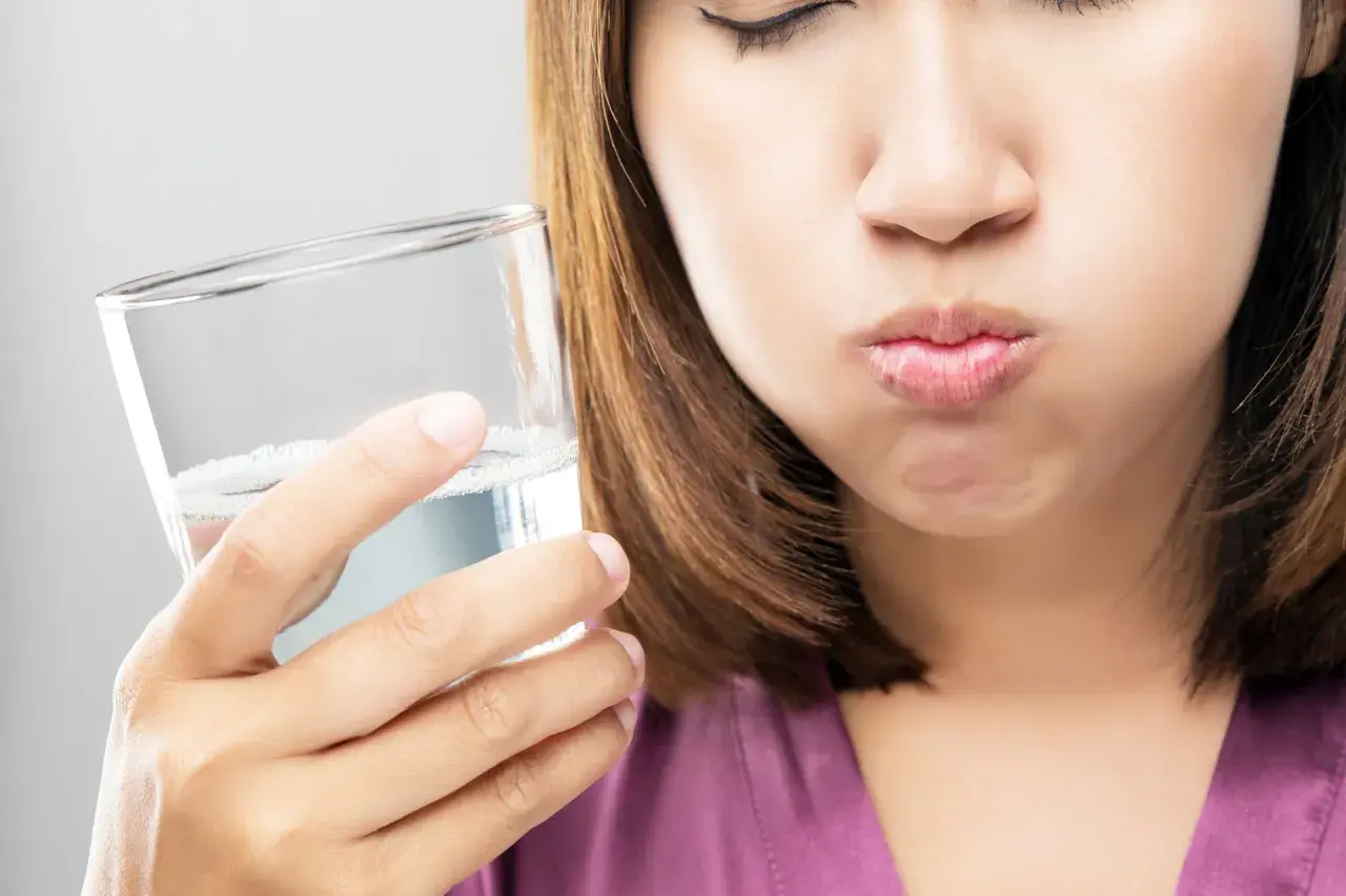 Frau mit geschlossenen Augen hält ein Glas Wasser und spült sich den Mund aus. Ein erfrischendes salzwasser am morgen Ritual.