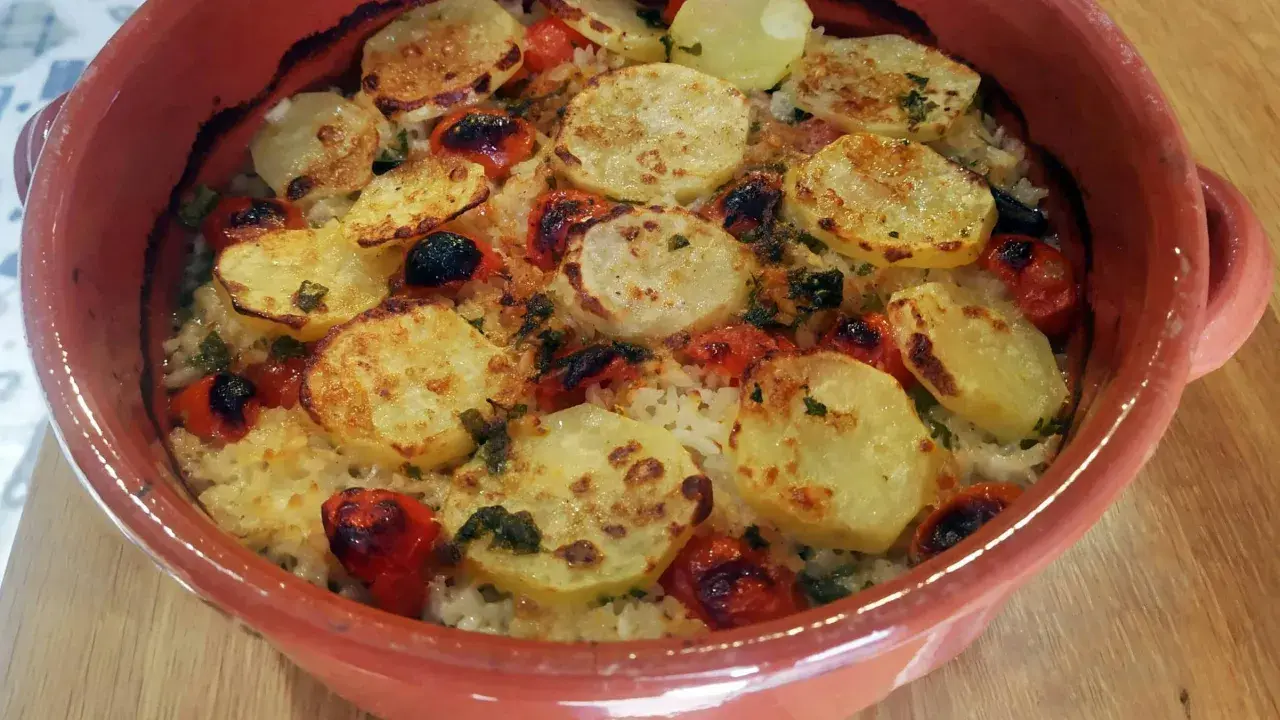 Piatto di riso patate e cozze cotto al forno, con pomodorini e erbe aromatiche, servito in una terrina di terracotta.