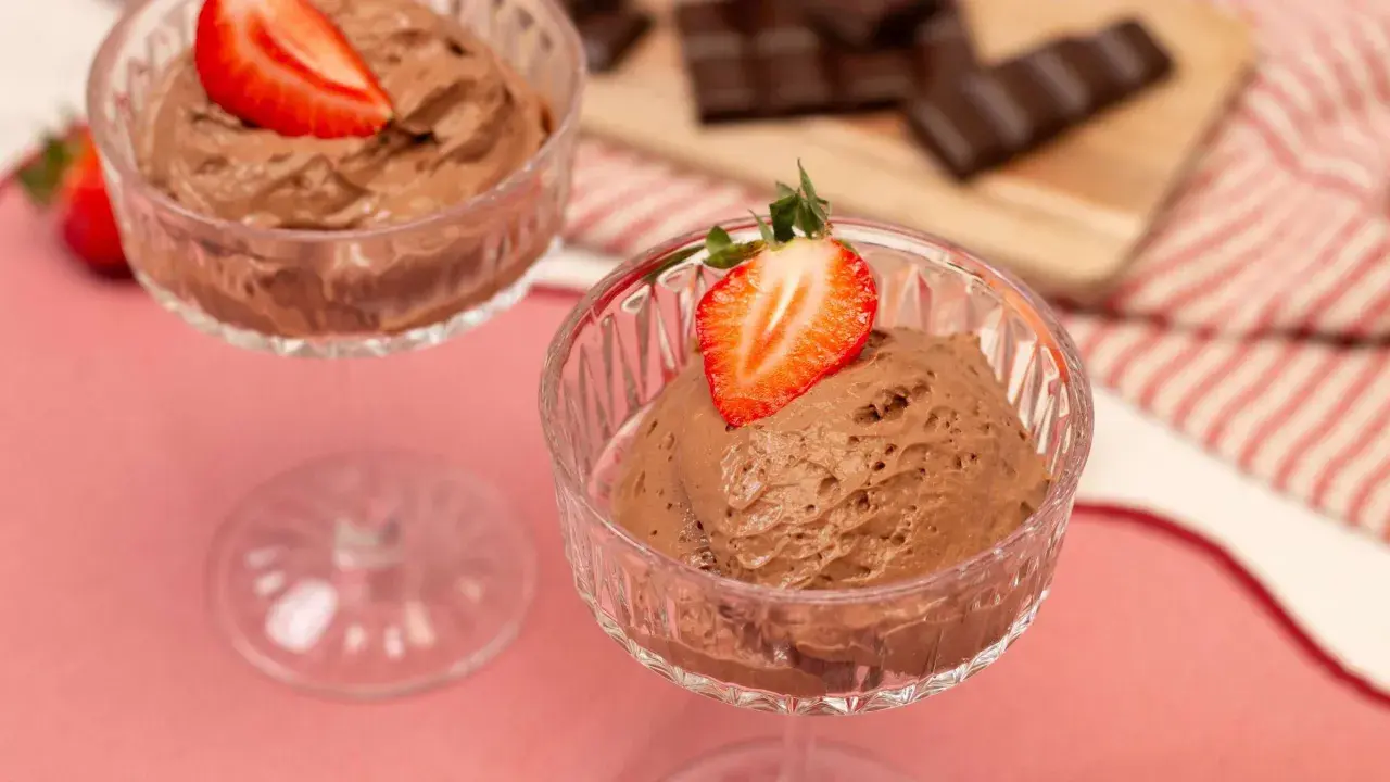 Zwei Gläser mit luftiger Schoko Mousse, garniert mit frischen Erdbeeren. Im Hintergrund liegen Schokoladenstücke.