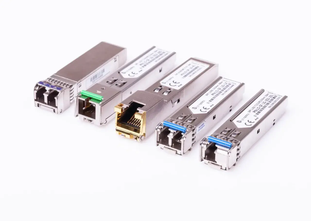 Różne moduły SFP i SFP+ w metalowych obudowach, niektóre z zielonymi lub niebieskimi złączami, inne z pozłacanym portem RJ45.