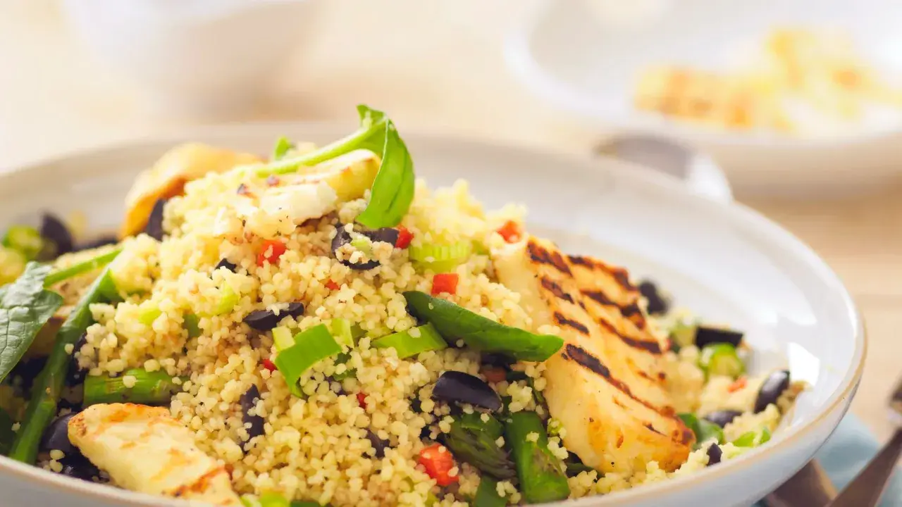 Un piatto colorato di cous cous con verdure miste, olive nere e cubetti di formaggio grigliato.
