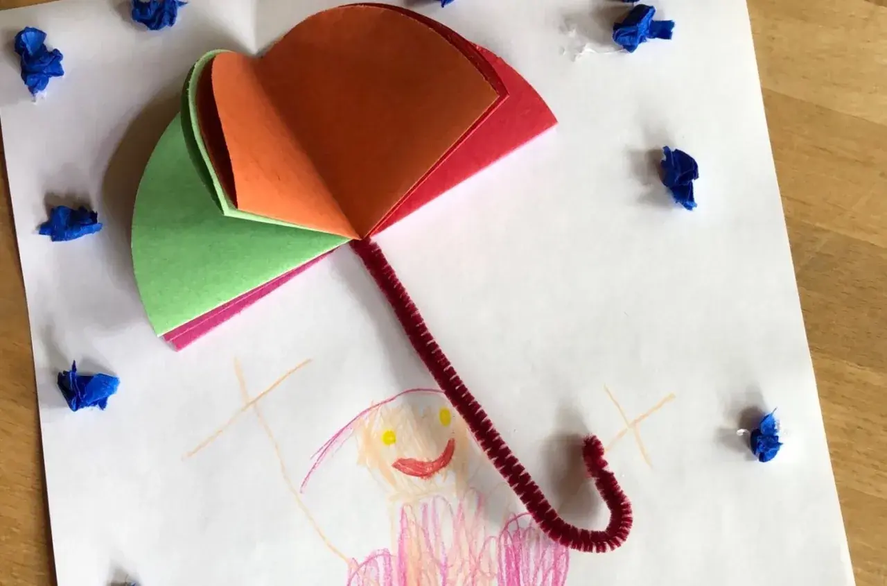 Buntes Papier und Pfeifenreiniger ergeben einen tollen Regenschirm zum Basteln. Kleine blaue Tupfer symbolisieren Regentropfen.