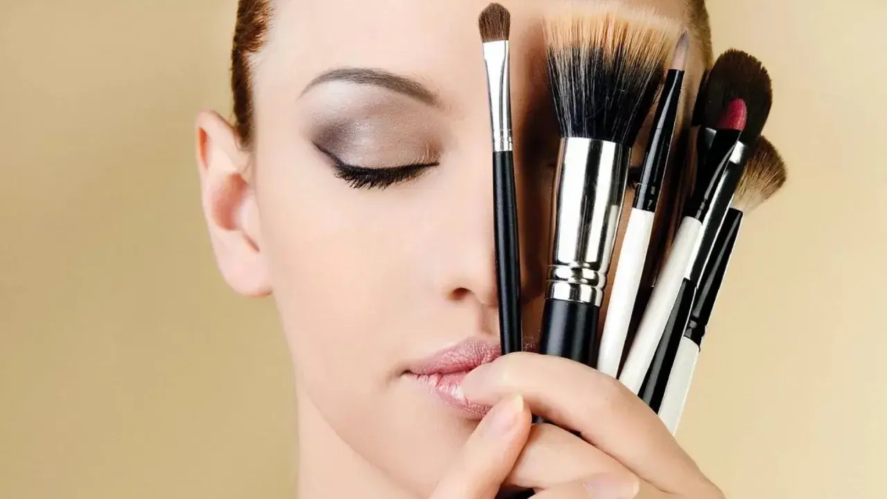 Mujer con ojos cerrados y varios pinceles de maquillaje, inspirando ideas de maquillaje.