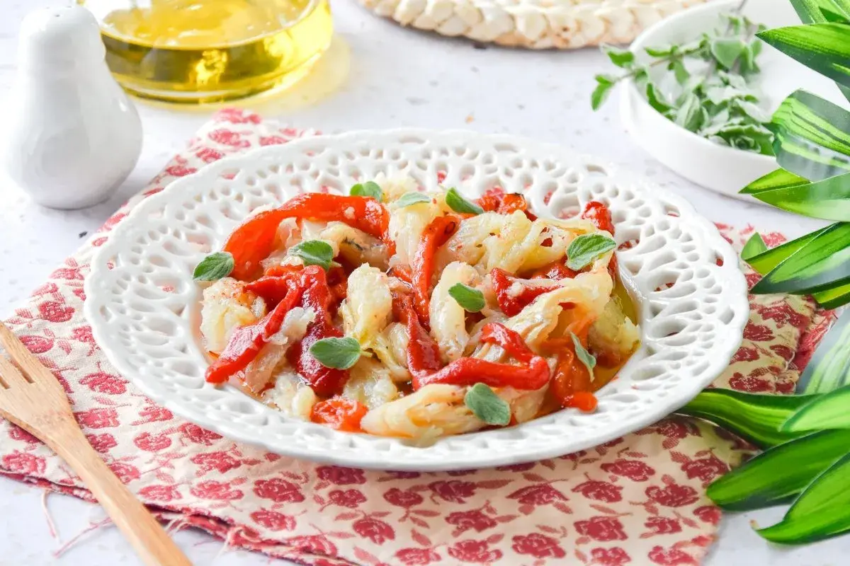 Deliciosa ensalada de bacalao con pimientos rojos asados y hierbas frescas, servida en un plato blanco decorado.