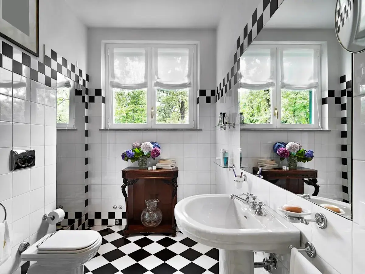 Un elegante bagno bianco e nero vintage con piastrelle a scacchi, un lavabo classico e un vaso di ortensie.
