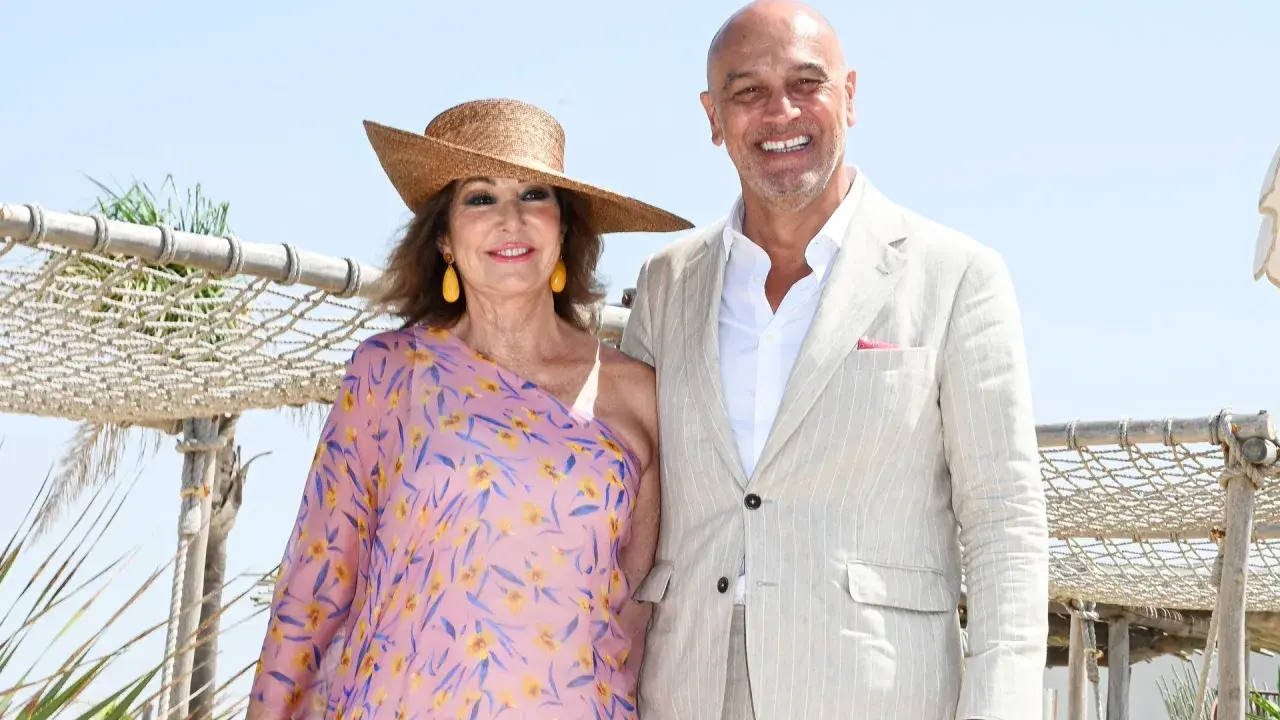 Ana Rosa Quintana y su marido celebran la boda de su hijo. Ella luce un vestido floral y sombrero, él un traje claro.