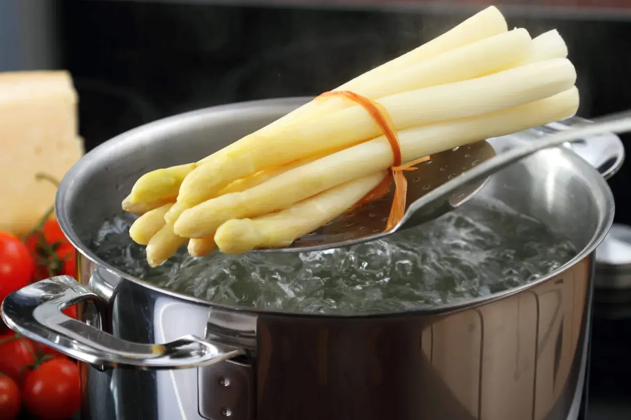 Un bouquet d'asperges blanches est plongé dans l'eau bouillante pour une cuisson parfaite.