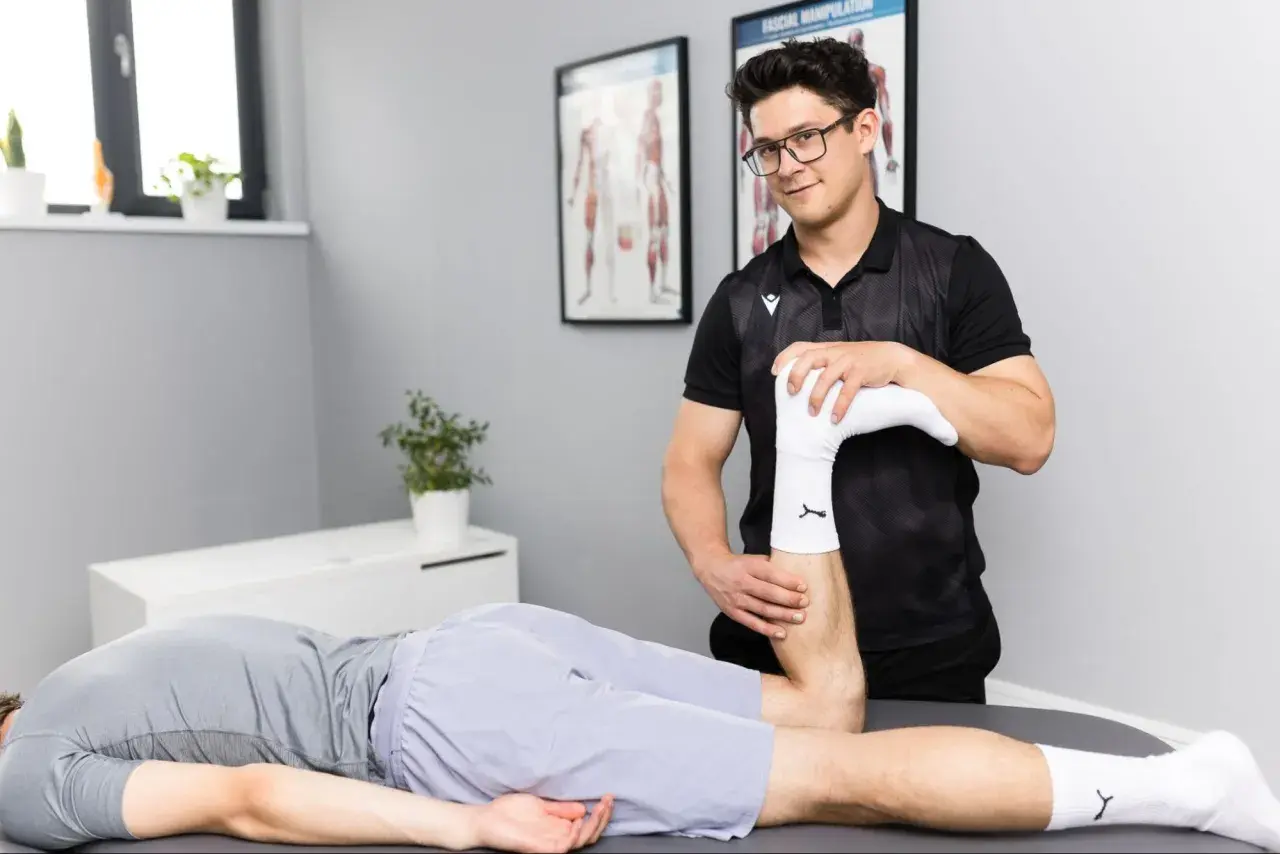Fizjoterapeuta wykonuje badanie nogi pacjenta leżącego na stole.