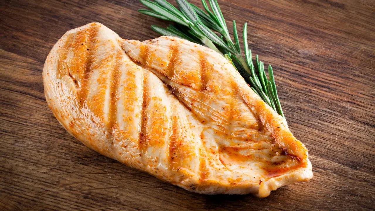Grillowana pierś kurczaka z rozmarynem na drewnianej desce. Pytanie: ile białka ma kurczak?