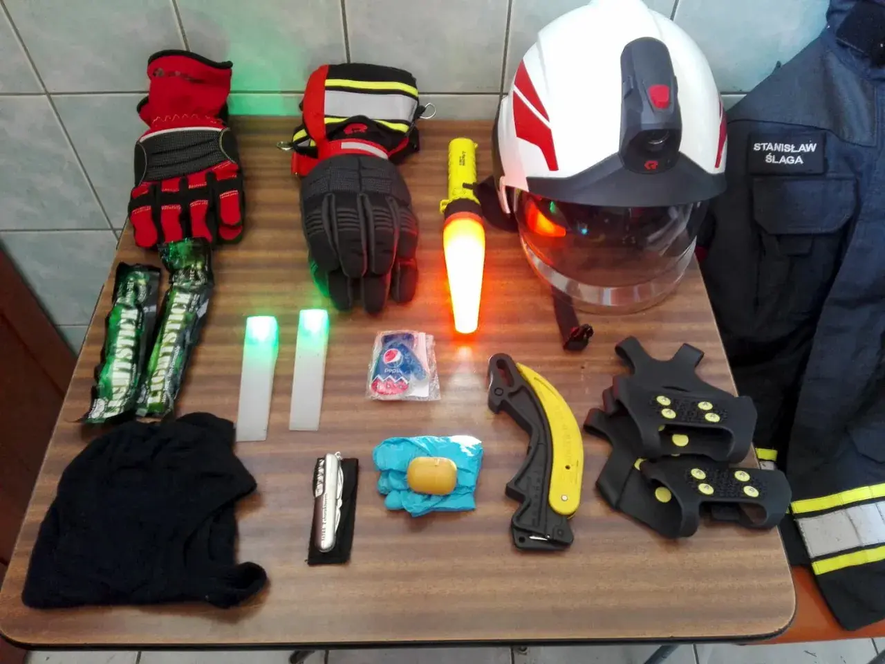 Na stole rozłożony sprzęt strażacki: rękawice, latarki, kask, nóż, raczki, kombinezon. Znajomość nazw sprzętu strażackiego jest kluczowa.