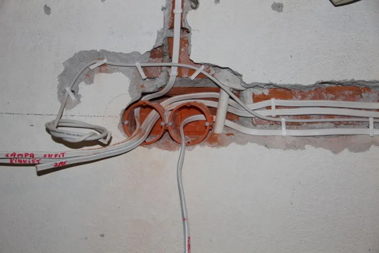 Rozpoczęta wymiana instalacji elektrycznej: widoczne puszki, przewody i fragmenty ceglanej ściany.