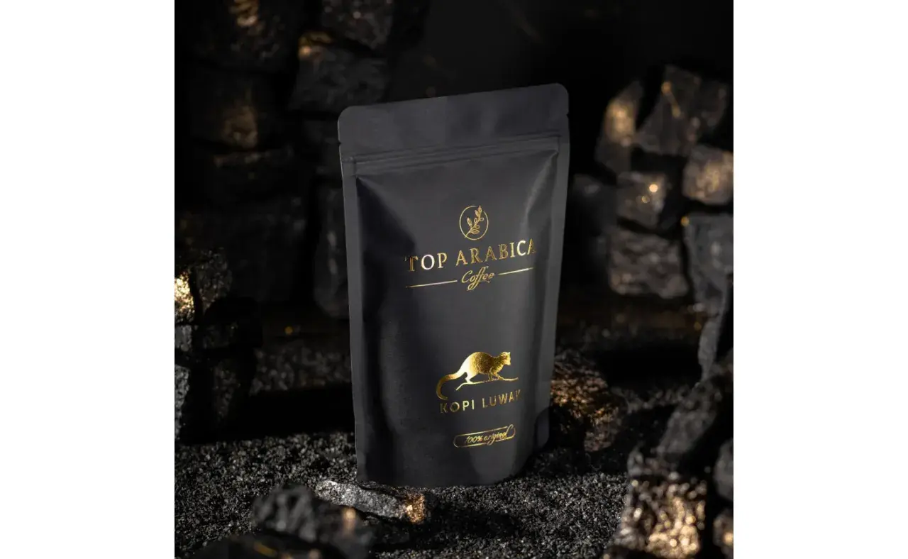 Czarna torebka z napisem "TOP ARABICA Coffee Kopi Luwak" i złotym rysunkiem zwierzęcia. To najdroższa kawa rozpuszczalna, otoczona węglem i złotymi drobinkami.