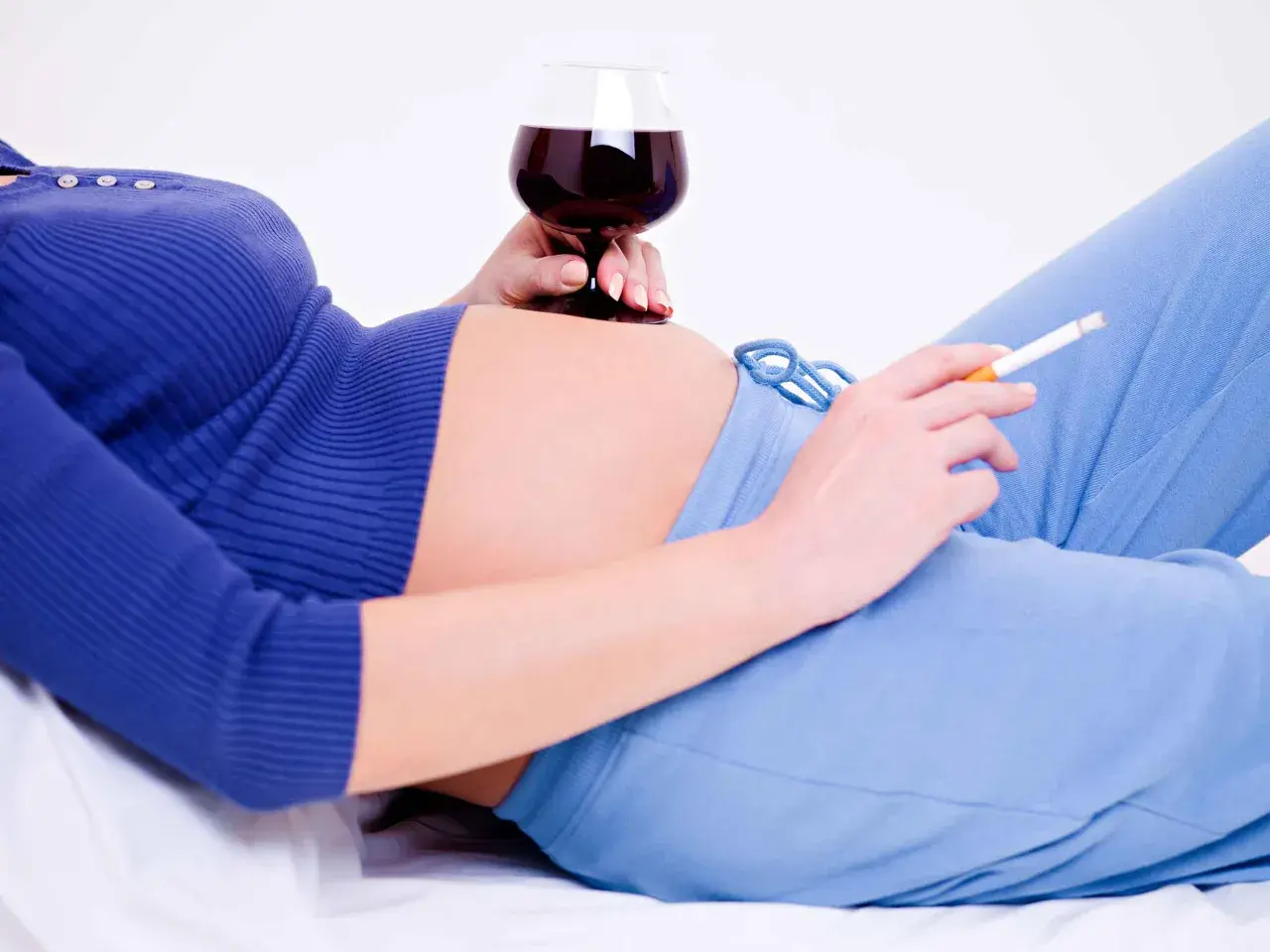 En gravid kvinna med en cigarett i ena handen och ett glas rödvin i den andra.