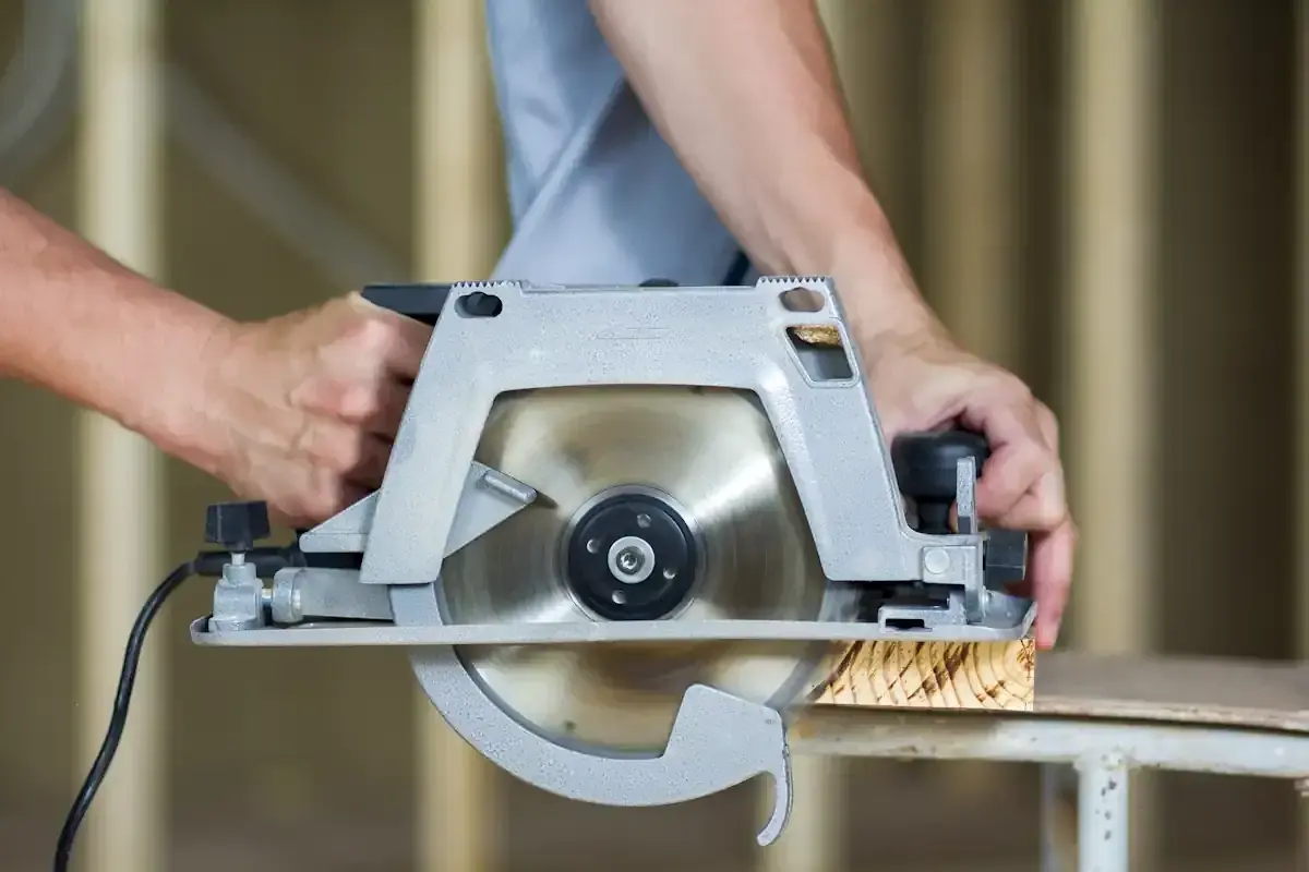 Mains d'un bricoleur utilisant une scie pour parquet stratifié, coupant une planche de bois.