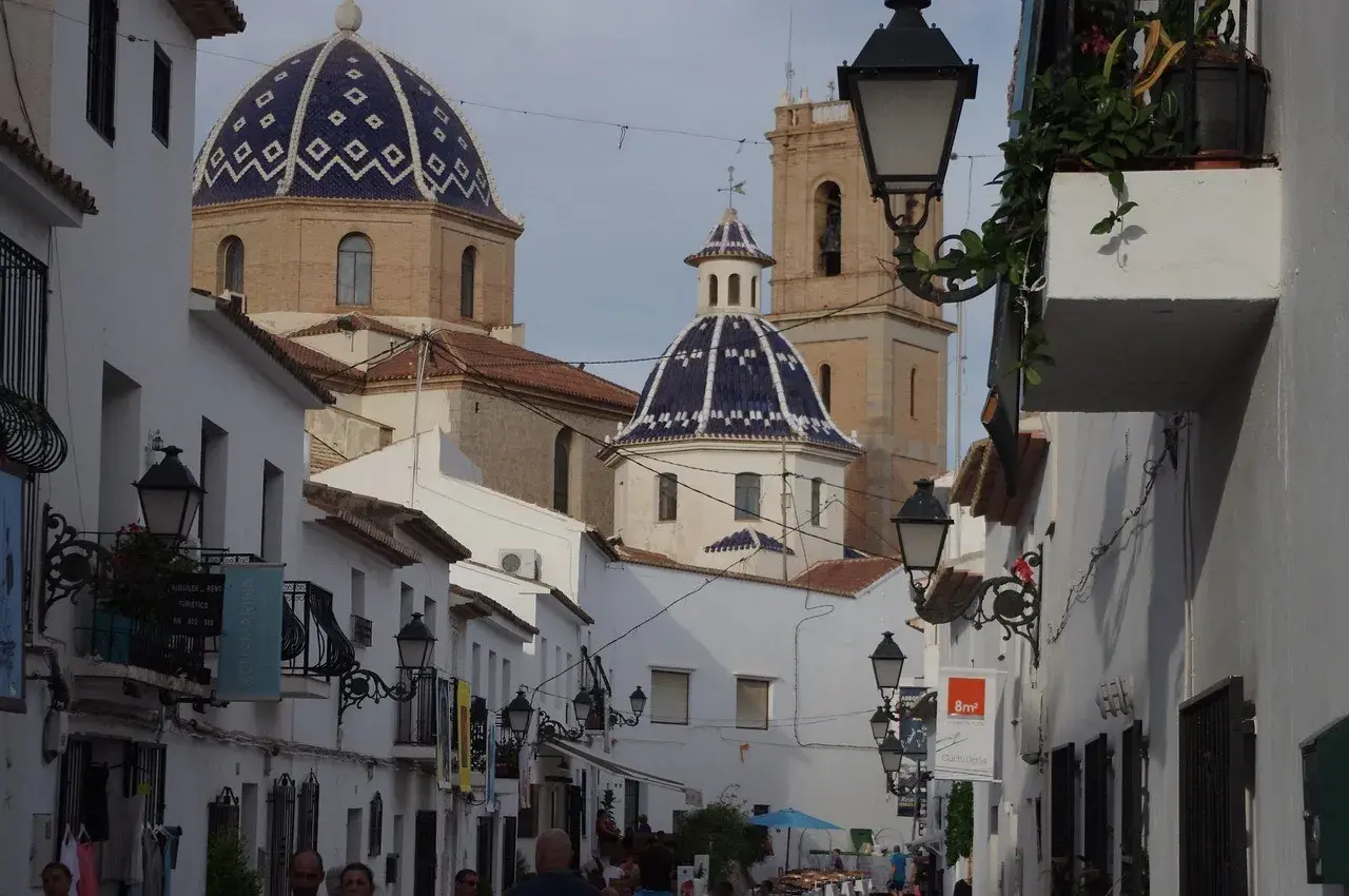 Calle estrecha con casas blancas y cúpulas azules, un ejemplo de los pueblos más bonitos de Alicante.