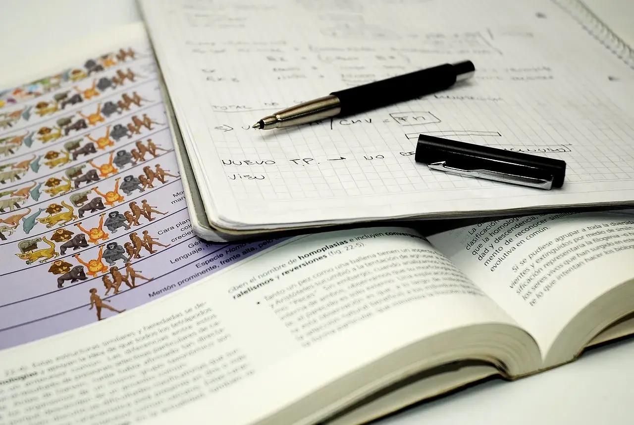 Cuaderno con notas, bolígrafo y libro abierto. El método Cornell se aplica en el estudio de la evolución, como muestra la imagen.