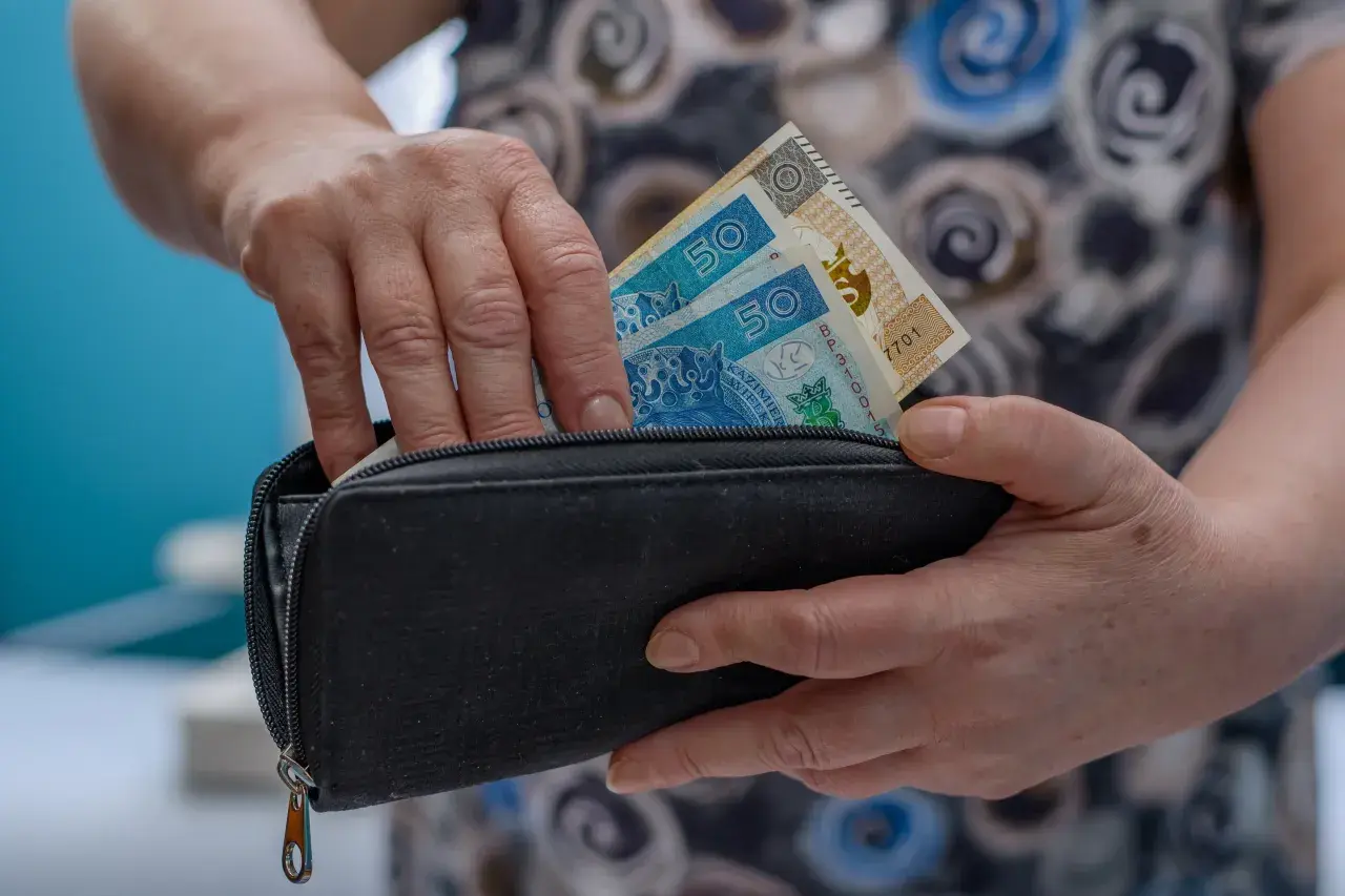 Dłonie chowają banknoty 50 zł do czarnego portfela. To może być początek oszczędzania na emeryturę, jak w funduszu Amundi Stars Silver Age.