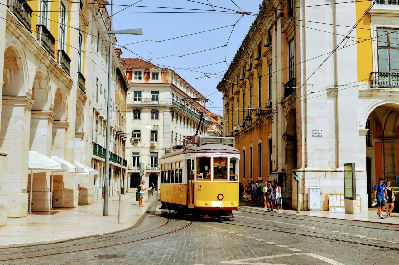 Gul lissabon spårvagn på kullerstensgata, omgiven av gul och vit arkitektur.